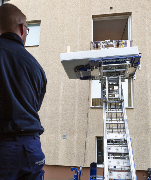 En flyttarbetare står vid en möbellift som används för att lyfta bohag upp till en balkong på ett flerbostadshus.